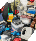 A cluttered collection of various items including storage boxes, a fan, luggage, and miscellaneous household objects piled together awaiting emergency restoration.
