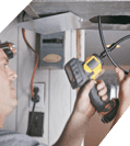 A man using a handheld device to perform emergency restoration on electrical wiring above his head, focusing intently on his task.