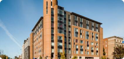 Modern brick apartment building under a clear blue sky, featuring large windows and a distinct corner tower, recently upgraded with emergency restoration.