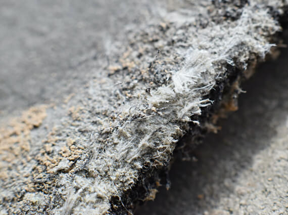 Close-up image of asbestos materials showing fibrous texture and frayed edges on a gray background, crucial for emergency restoration assessments.