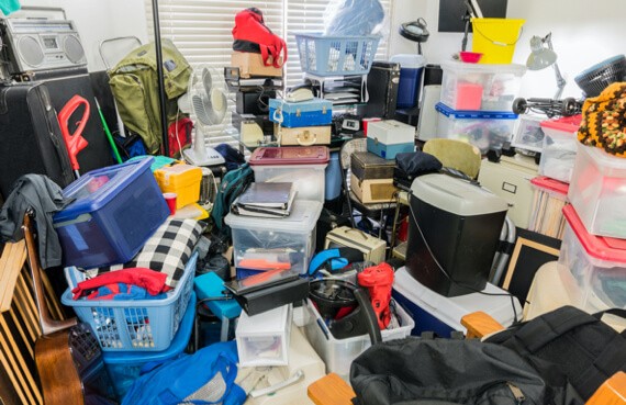 A cluttered room filled with assorted items like containers, boxes, bags, and various household goods stacked in a disorganized manner awaiting emergency restoration.