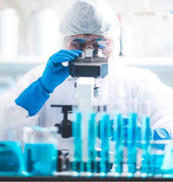 A scientist in a cleanroom suit using a microscope in an emergency restoration laboratory, surrounded by blue-tinted glassware.