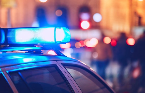 Emergency blue light bar on top of a patrol car illuminated at night with blurred city street lights in the background.